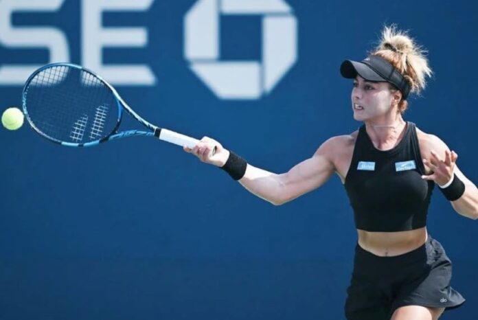 Mexican professional tennis player Renata Zarazua in a black tennis outfit and her blonde hair tired up in a bun, hitting a tennis ball with a forehand swing during a match.