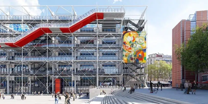 Facade of the Pompidou Centre in Paris, featuring a grid like design with terraces and a rising deck in red and white, facing a wide set of stairs and plaza in front of the building and to its left.