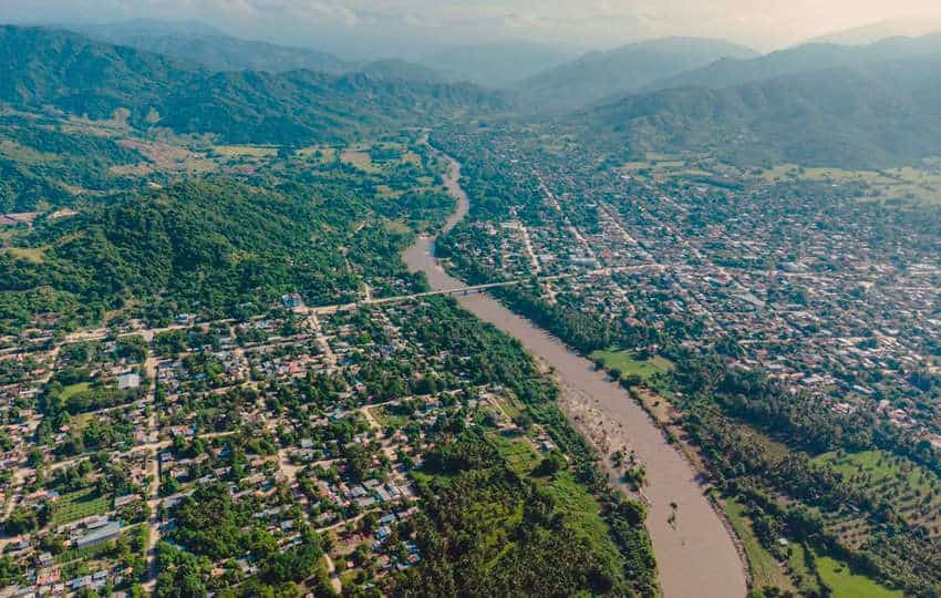 Aerial view of a rural community alongside a winding river and surrounding by forest.