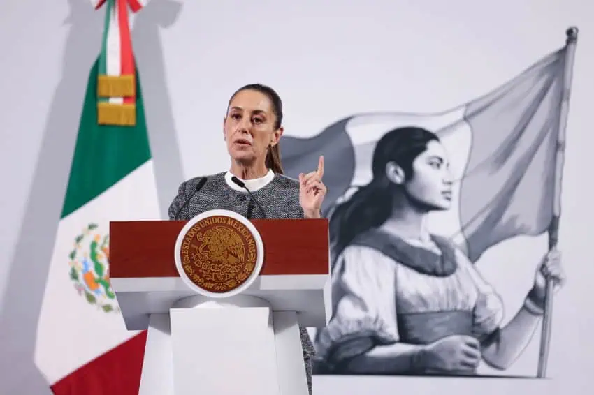 President Sheinbaum of Mexico at the presidential podium during a press conference in the National Palace. She is holding one finger up to make a point.