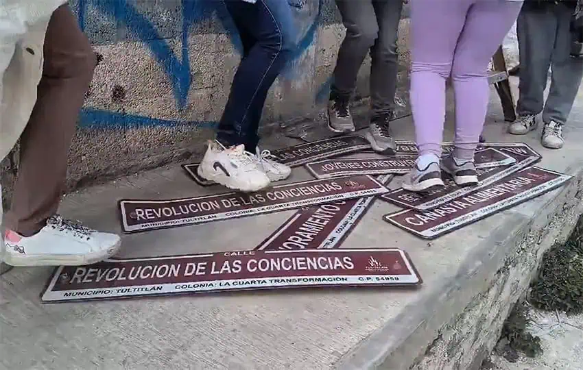 Feet stamp on street signs in the Colonia 4T with names like "Revolución de las Consciencias" inspired by former President AMLO