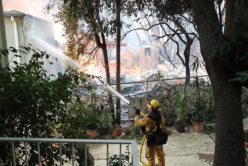 A firefighter sprays a mostly extinguished building with water in the Pacific Palisades, Los Angeles