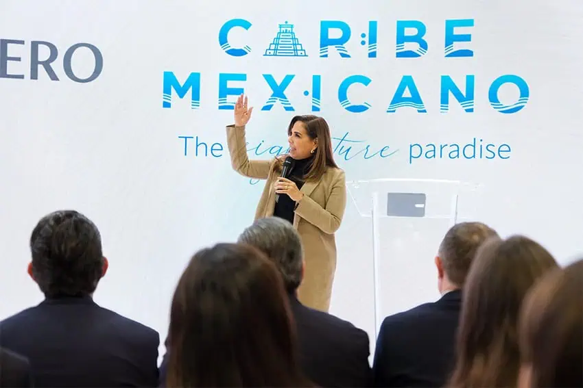 Quintana Roo Gov. Mara Lezama speaks on a stage in front of a banner reading "Caribe Mexicano."