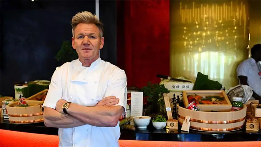 Chef Gordon Ramsay stands in front of a table full of food