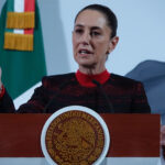 President Sheinbaum stands in front of a Mexican flag at her morning press conference