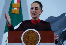 President Sheinbaum stands in front of a Mexican flag at her morning press conference