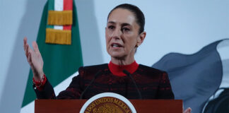President Sheinbaum stands in front of a Mexican flag at her morning press conference