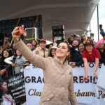 Mexican President Claudia Sheinbaum takes a selfie in front of a crowd holding signs thanking her
