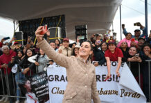 Mexican President Claudia Sheinbaum takes a selfie in front of a crowd holding signs thanking her