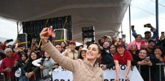Mexican President Claudia Sheinbaum takes a selfie in front of a crowd holding signs thanking her