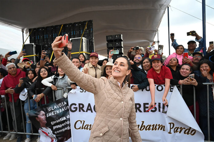 Mexican President Claudia Sheinbaum takes a selfie in front of a crowd holding signs thanking her