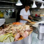 A Mexico City taquero prepares food in the background, with a pile of roasted nopales, meat and vegetables in the foreground