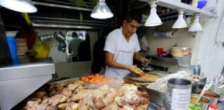 A Mexico City taquero prepares food in the background, with a pile of roasted nopales, meat and vegetables in the foreground