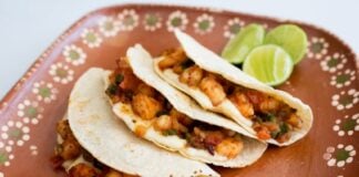 Three tacos gobernador on a brown ceramic plate with limes in background