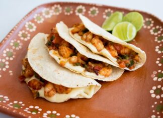 Three tacos gobernador on a brown ceramic plate with limes in background