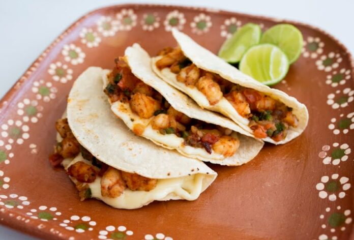 Three tacos gobernador on a brown ceramic plate with limes in background