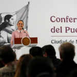 President Claudia Sheinbaum of Mexico at her daily press conference, standing at the presidential podium smiling out at reporters.