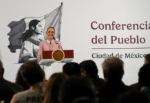 President Claudia Sheinbaum of Mexico at her daily press conference, standing at the presidential podium smiling out at reporters.