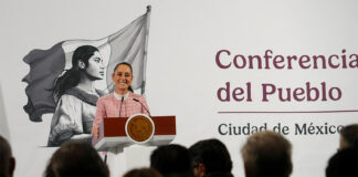 President Claudia Sheinbaum of Mexico at her daily press conference, standing at the presidential podium smiling out at reporters.