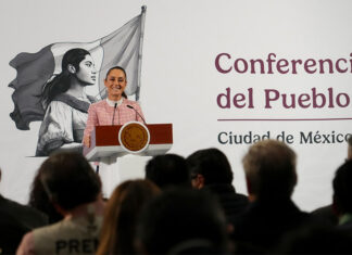 President Claudia Sheinbaum of Mexico at her daily press conference, standing at the presidential podium smiling out at reporters.