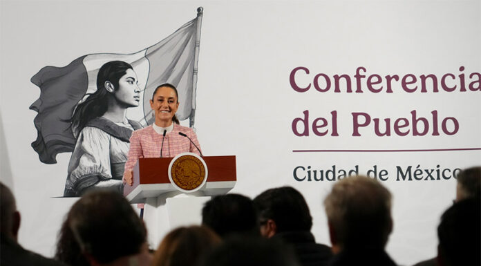 President Claudia Sheinbaum of Mexico at her daily press conference, standing at the presidential podium smiling out at reporters.