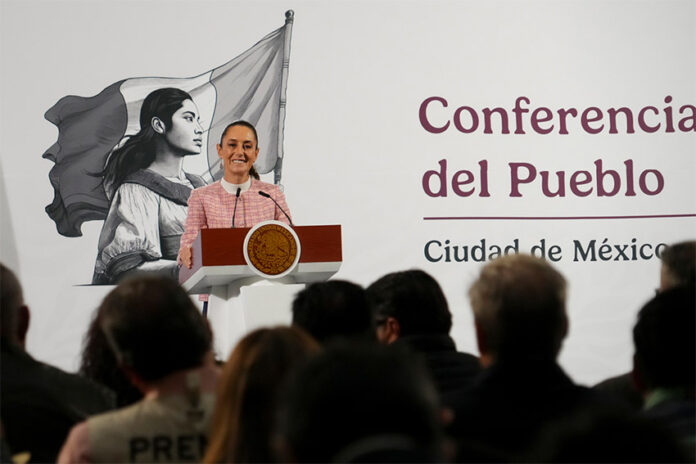 President Claudia Sheinbaum of Mexico at her daily press conference, standing at the presidential podium smiling out at reporters.