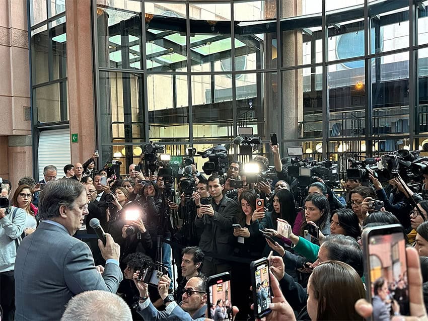 Marcelo Ebrard speaks into a microphone surrounded by a crowd of journalists at the American Society of Mexico