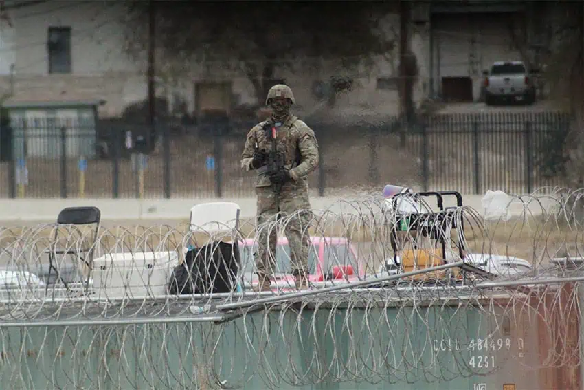 A U.S. soldier stands guard near the Mexico border, behind rows of barbed wire