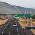 A federal divided highway in Mexico with one lane in each direction. Cars are traveling in both directions near a highway signs for Cuautla and Cuernavaca and an exit sign for Izucar de Matamoros and Atlixco.