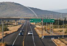 A federal divided highway in Mexico with one lane in each direction. Cars are traveling in both directions near a highway signs for Cuautla and Cuernavaca and an exit sign for Izucar de Matamoros and Atlixco.