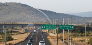 A federal divided highway in Mexico with one lane in each direction. Cars are traveling in both directions near a highway signs for Cuautla and Cuernavaca and an exit sign for Izucar de Matamoros and Atlixco.
