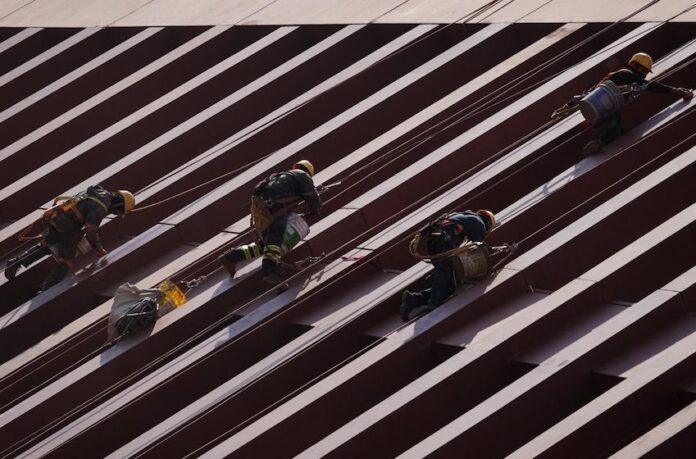 Men in construction gear in Mexico City scaling a row of steel girders on a building.