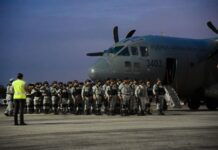 National Guardsmen in gray uniforms at dawn, standing in formation next to a Mexican Airforce carrier jet, waiting to board.