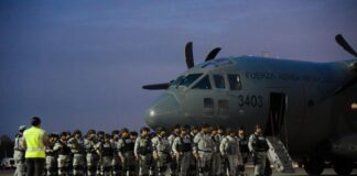 National Guardsmen in gray uniforms at dawn, standing in formation next to a Mexican Airforce carrier jet, waiting to board.