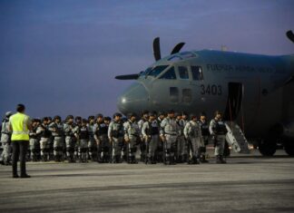 National Guardsmen in gray uniforms at dawn, standing in formation next to a Mexican Airforce carrier jet, waiting to board.