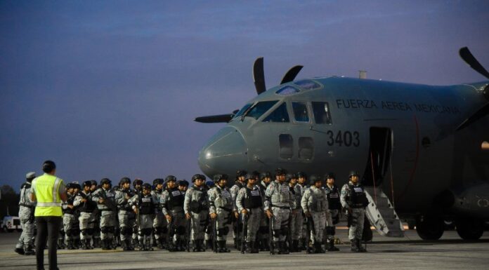 National Guardsmen in gray uniforms at dawn, standing in formation next to a Mexican Airforce carrier jet, waiting to board.