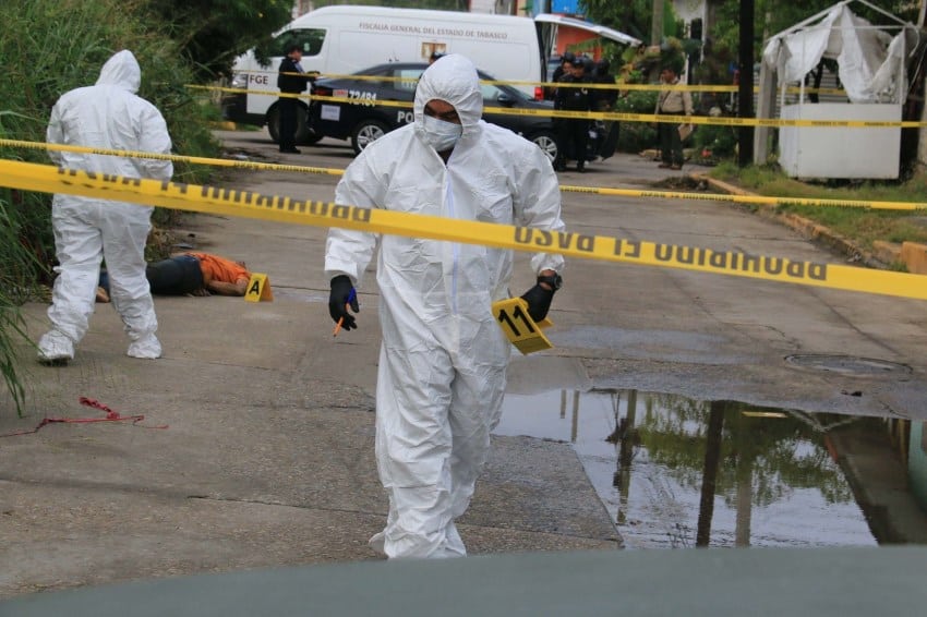 Forensic experts covered from head to foot in white protective gear marking a crime scene with bodies in the street of Villahermosa, Mexico.