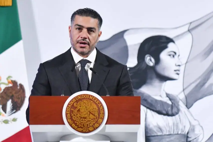 Middle aged Mexican official standing at the presidential podium in the National Palace speaking to reporters during a press conference.