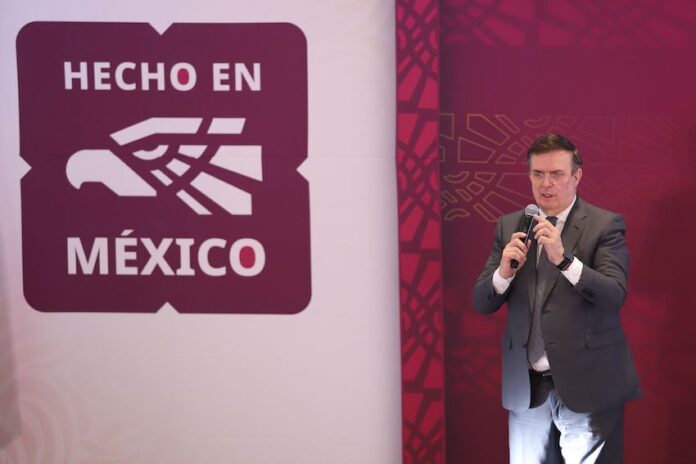 Mexico's Economy Minister Marcelo Ebrard standing on a stage and holding a microphone with the 