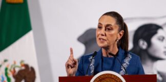 Mexico's President Claudia Sheinbaum at her daily press conference. She is holding up a finger as she makes a point to reporters behind a podium in the National Palace press briefing room