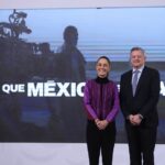 President Sheinbaum at her daily press conference standing and posing for a picture with Netflix CEO Ted Sarandos. They are standing in front of a projection screen with a still of a crew filming a movie