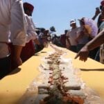 People stand around a table with a long taco that stretches to the horizon