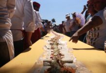 People stand around a table with a long taco that stretches to the horizon