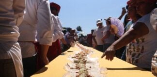 People stand around a table with a long taco that stretches to the horizon