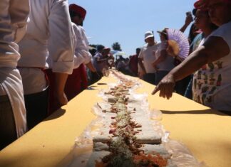 People stand around a table with a long taco that stretches to the horizon