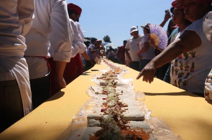 People stand around a table with a long taco that stretches to the horizon