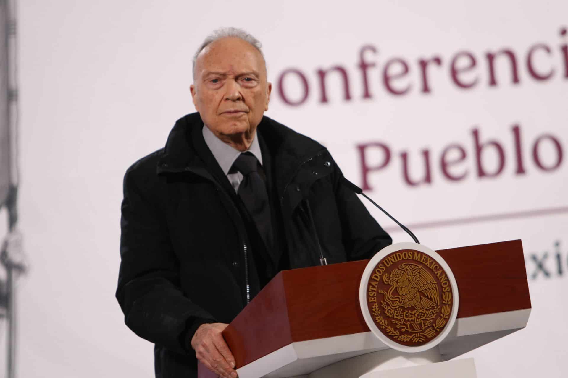 El Fiscal General de México, Alejandro Gertz Manero, un hombre anciano con traje y corbata oscuros, con una parka negra sobre eso, se encuentra en el podio presidencial en el Palacio Nacional de la Ciudad de México, informando sobre seguridad en México.