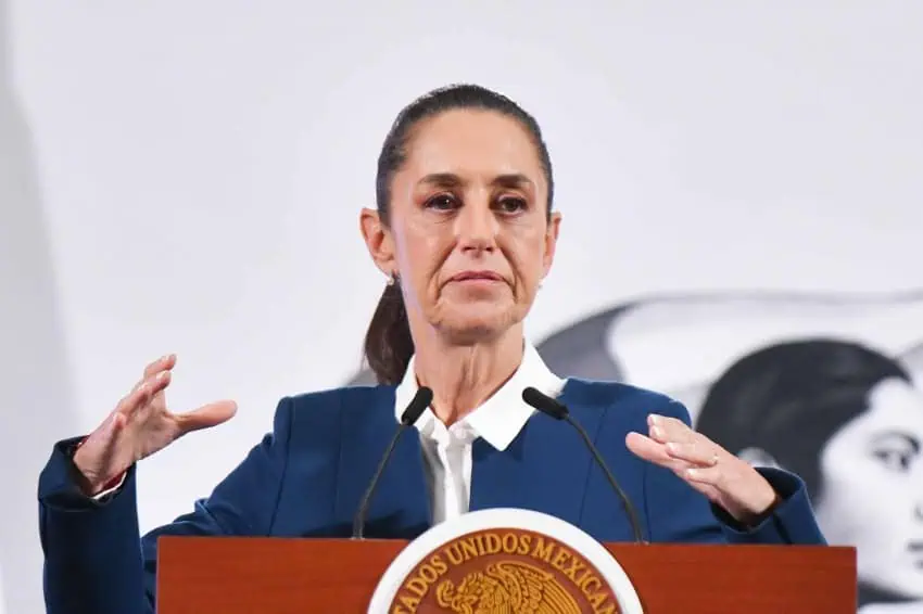 President Claudia Sheinbaum at her daily press conference, standing behind a podium with her hands at the height of her shoulders. She looks as if she is describing something with her hands.