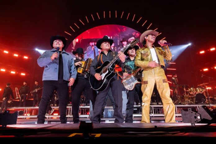 The band Grupo Firme plays together on a stage