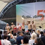 Band playing onstage at the International Cervantino Festival in 2024. The band of all men and one woman are dressed in traditional Mexican shirts, black pants and white campesino hats. One of the man is holding his hat up and out at the audience.